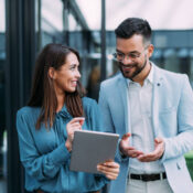 Shot of two confident colleagues walking and talking next to an office building. Businessman and businesswoman in meeting using digital tablet and discussing business strategy. Creative business persons discussing new project and sharing ideas while walking in front of their office building.