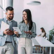 Shot of a two confident business persons talking in the work place. Two colleagues using a digital tablet while walking in a modern office. Businessman and businesswoman in meeting discussing business strategy. Business coworkers working together in the offic
